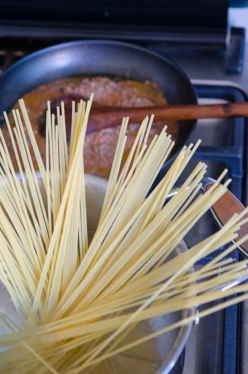 Spaghetti kochen in einem Topf, im Hintergrund eine Pfanne in der Bolognese Sauce aufgewärmt wird.